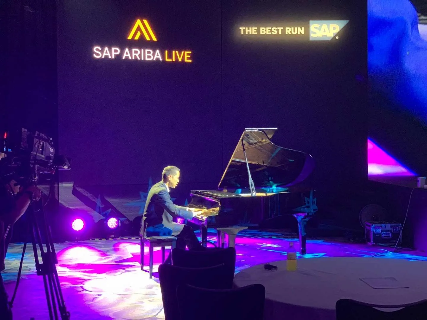 A pianist playing a grand piano on a lit stage at a corporate event