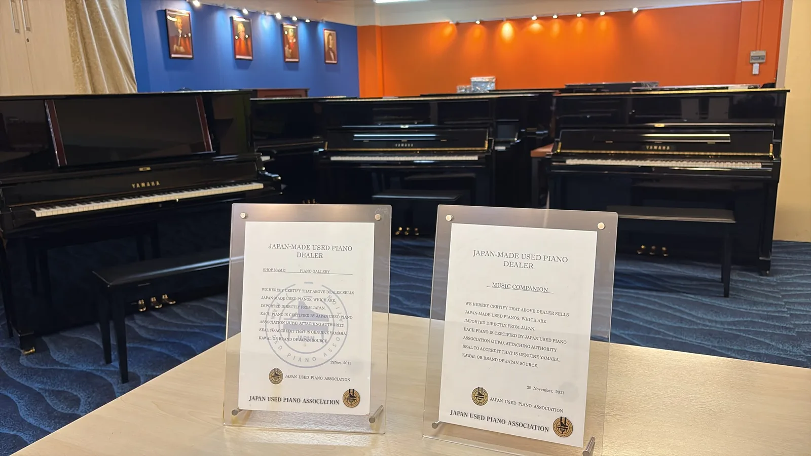 Two Japan Used Piano Association dealer certificates standing on a table in the viewing gallery, one naming Piano Gallery and one naming Music Companion, both dated 29 November 2011