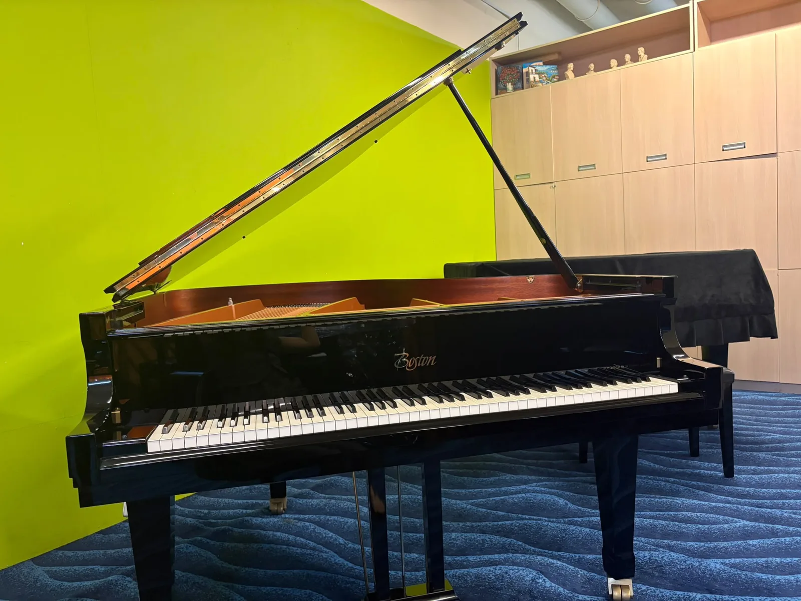 A Boston grand piano with the lid raised in a room with a green wall