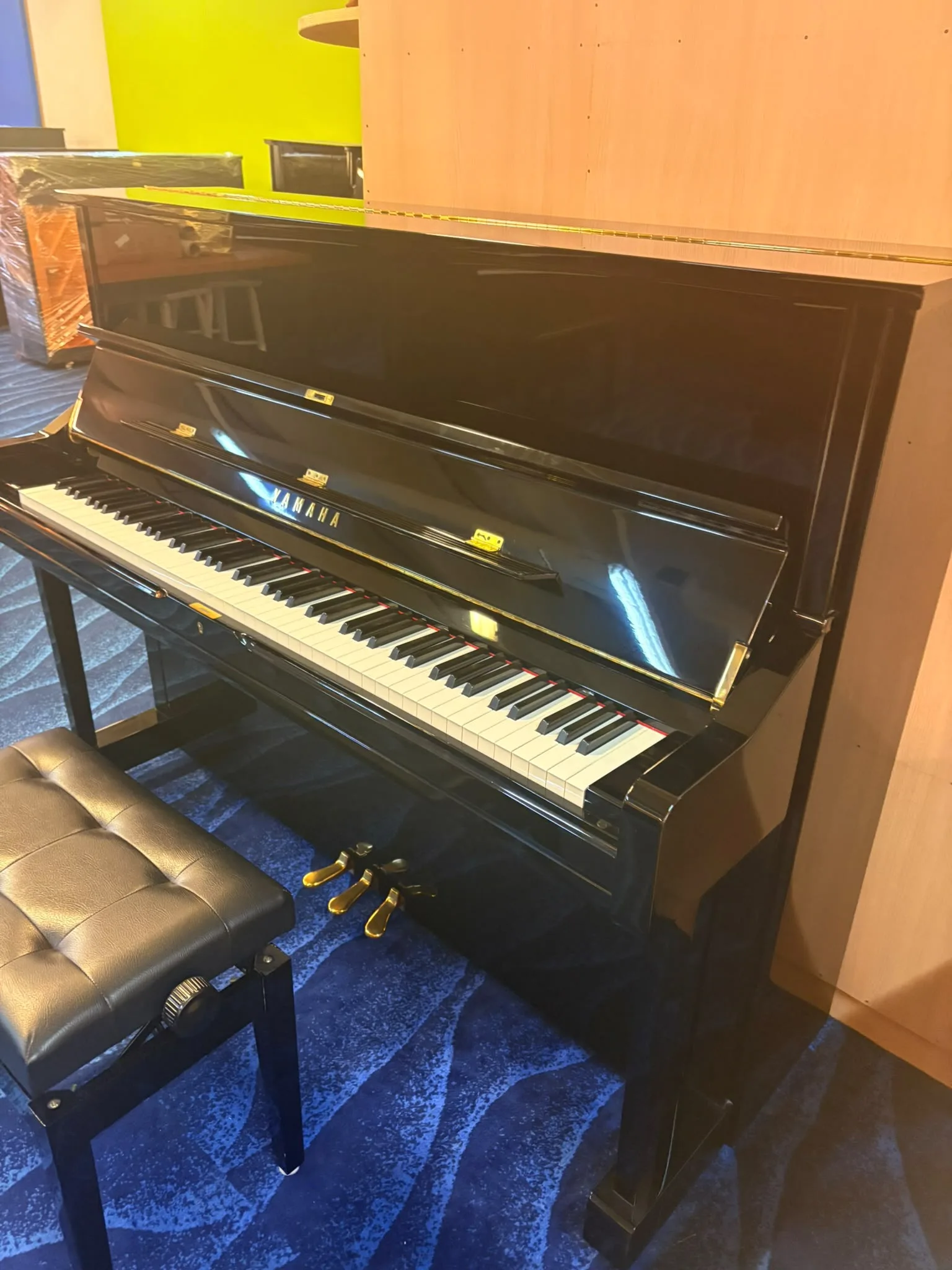 A black upright piano with a leather bench in the viewing gallery