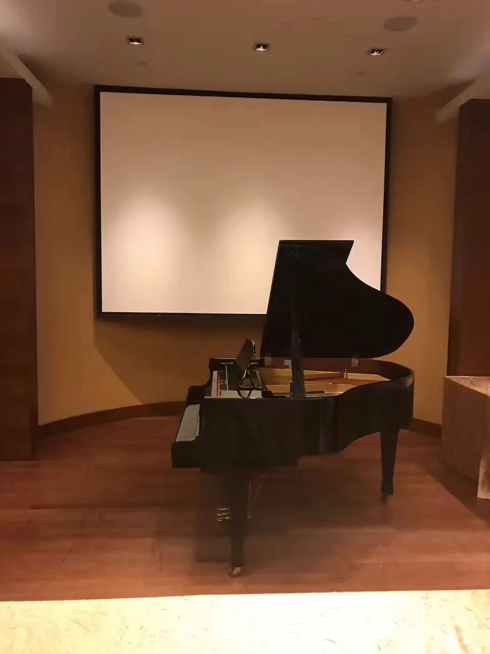 A grand piano placed below a projection screen in an auditorium