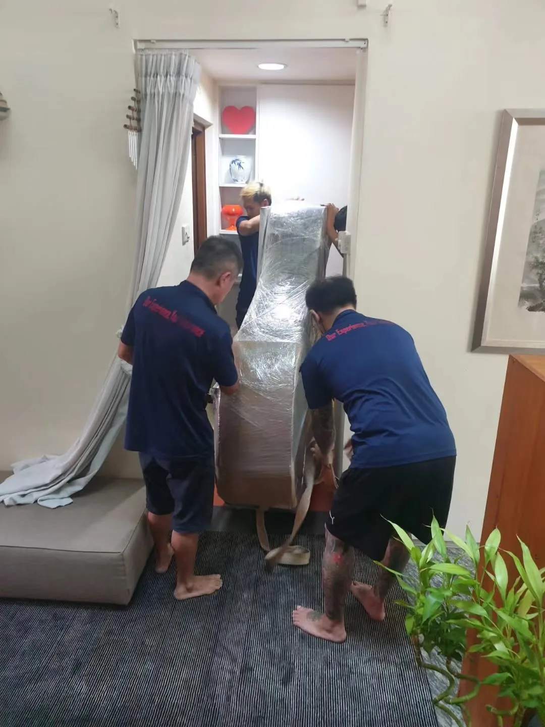 Two movers carrying a wrapped piano into a home