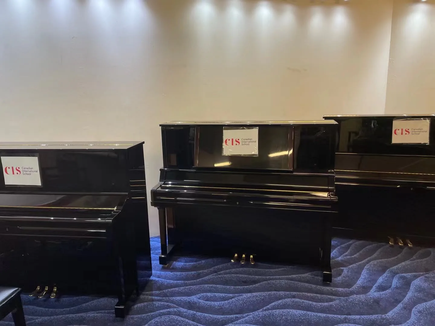 Three upright pianos on the viewing gallery floor labelled for Canadian International School