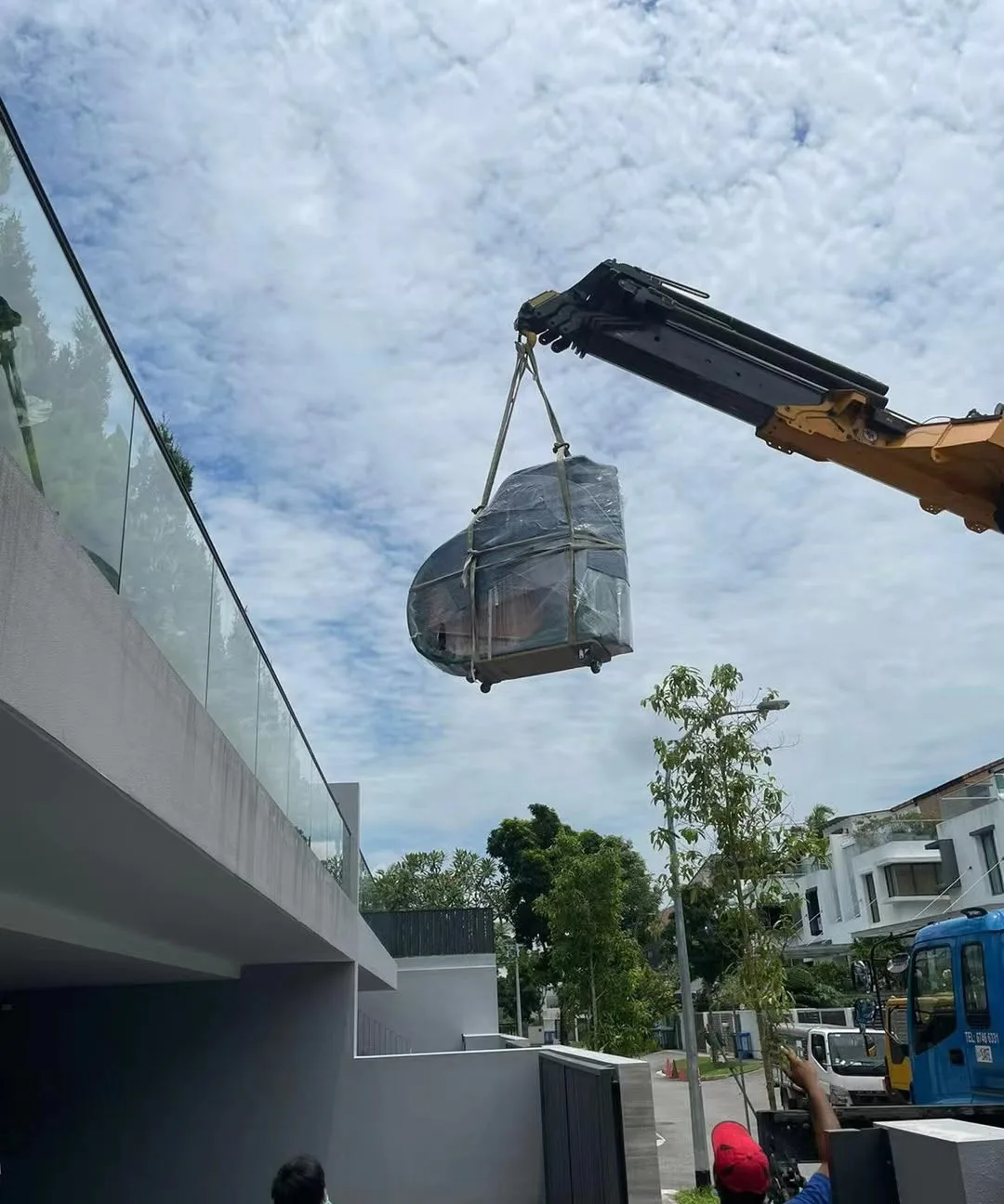 A crated piano slung from a crane above a house during a delivery