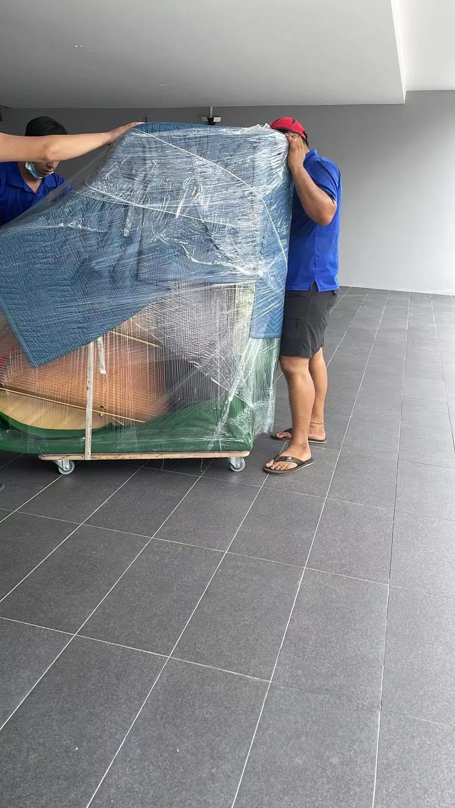 A wrapped piano crossing a lift lobby on a dolly