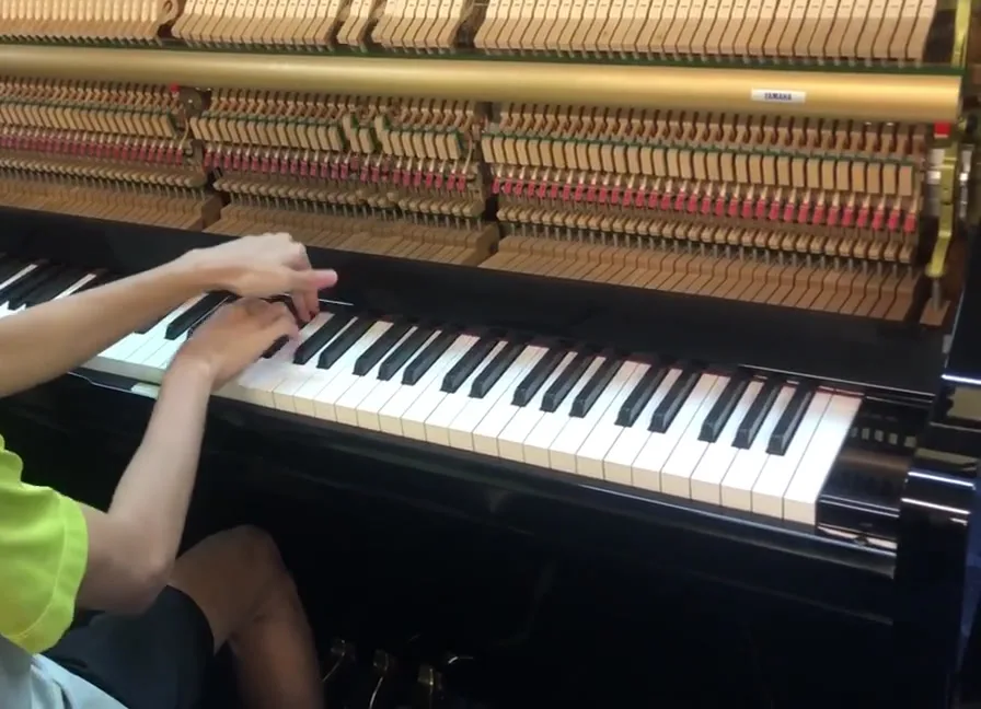 Hands at the keys of an upright piano with the top board off and the action exposed